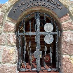 Schmiedeeisernes Denkmal der Heiligen mit Attributen auf dem Gitter. St. Birgitta von Schweden  Stab, St. Benedikt  Medaillon