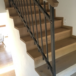 Geschmiedetes Geländer für die Treppe im Innenraum – einfaches Geländer mit einem hölzernen Handlauf Geschmiedetes Geländer für die Treppe im Innenraum – einfaches Geländer mit einem hölzernen Handlauf