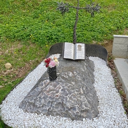 Ein Kreuz in Form eines Olivenbaums, auf einem Felsen platziert, mit einem offenen Buch, das ber den Verstorbenen schreibt